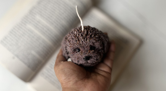 A handmade, brown Poochie Dog Candle from Candlesence Online, held in a hand to show its detailed, textured design.